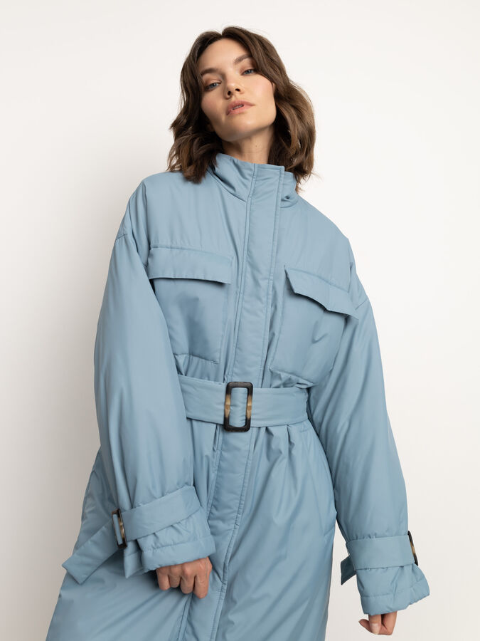 Куртка Удлинённая куртка пыльно-голубого цвета. Изготовлена на утеплённой подкладке. Модель свободного прямого силуэта, который можно самостоятельно регулировать поясом из комплекта. Спереди на куртке